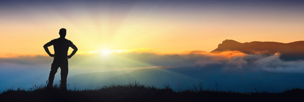 Man standing at the top of a hill looking towards the horizon